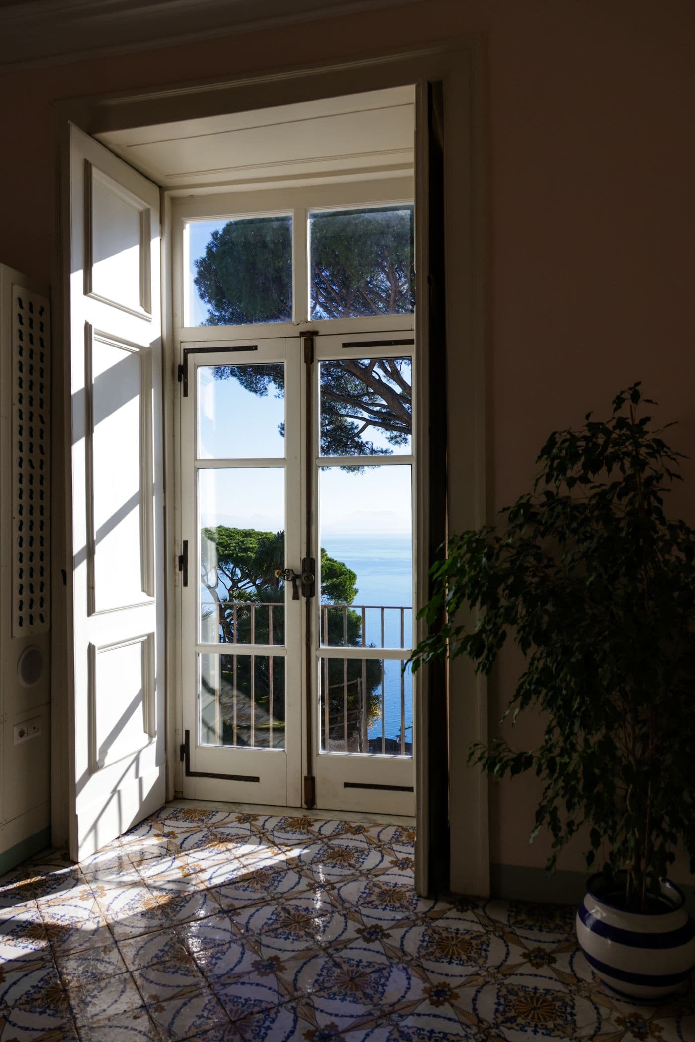 Sunlight through an open villa balcony door overlooking the sea.